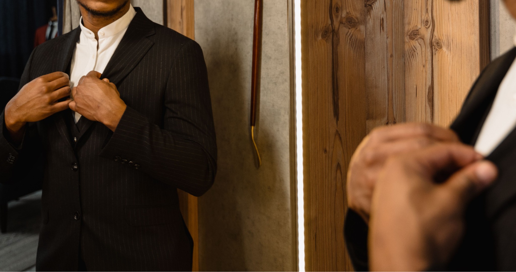 A person adjusting a dark suit jacket in front of a mirror